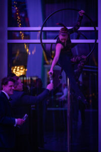 A woman on a circus apparatus pours champagne into a guest's class